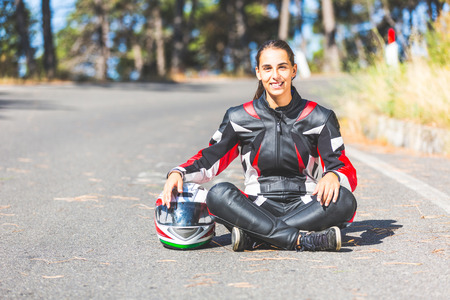 Motorcycle rider sitting in the street. There is a girl with motorcycle clothing and an helmet. She...