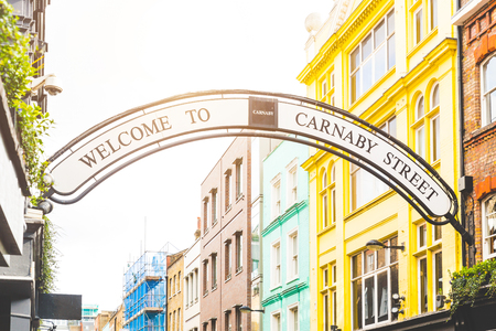 Carmaby street sign in London with some colorful houses on background and sun beams from top. This is a famous place in London, with many tourists visiting every day.のeditorial素材