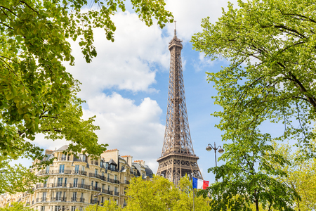Paris view with the Eiffel Tower, a French flag, some trees and a typical Parisian building. Travel and architecture concepts about the capital city of France.の写真素材