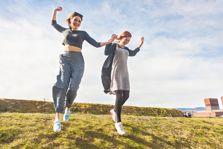 Two girls running down a hill in Oslo, holding hands and laughing. They are having fun together on a sunny spring day. Lifestyle and friendship concepts.の写真素材