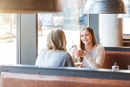 Two beautiful young women in a cafe, drinking coffee and latte macchiato and talking.の写真素材