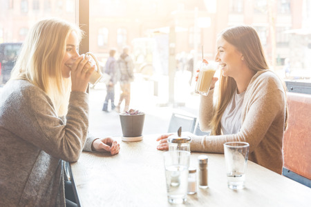 Two beautiful young women in a cafe, drinking coffee and latte macchiato and talking.の写真素材