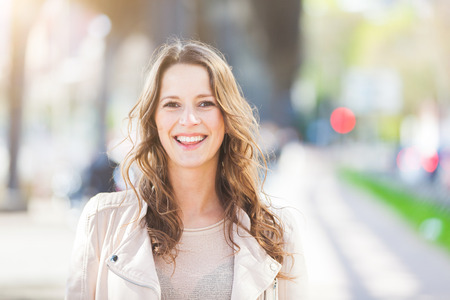 Portrait of a beautiful young woman in Hamburg. She is caucasian, on her early twenties, brunette with long hair. Looking at camera and smiling. Smart casual clothes, blurred urban backgroundの写真素材