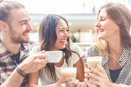 Multiracial group of friends having a coffee together. Two women and a man at cafe, talking, laughing and enjoying their time. Lifestyle and friendship concepts with real people models.の写真素材