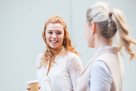 Two women walking in the city and talking. Young businesswomen in London taking a break from office on a sunny day. City and work lifestyle concepts with real people.の写真素材