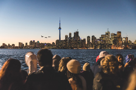 TORONTO, CANADA - OCTOBER 13, 2016: People on the ferry boat from Toronto islands to downtown looking at the skyline and taking pictures with phones at sunsetのeditorial素材