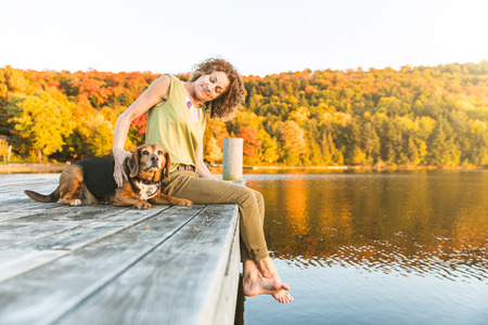 Woman and dog relaxing on the dock. Autumn colors, unstaged situation with candid model and her dog. Relaxation and friendship concepts.の写真素材