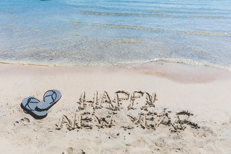 Happy new year writing on the sand at seaside. Best wishes for a happy new year from holiday destination. Empty space to add text on the top of the photo.の写真素材