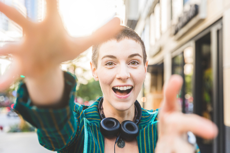 Young woman portrait, looking at and catching the camera with hands. Smiling and happy face of a woman with short hair having fun in the city.の写真素材