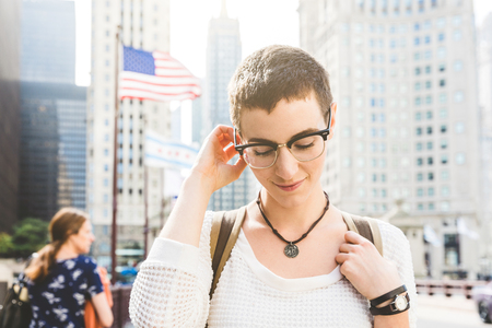 Young woman portrait in Chicago with USA flag on background. Woman with short hair and eyeglasses looking down, shyness and lifestyle concepts.の写真素材