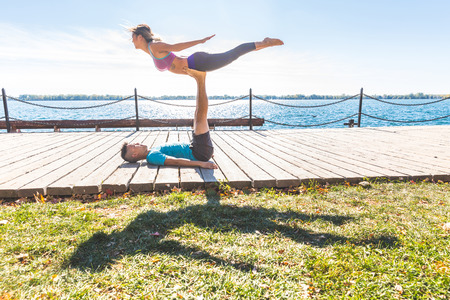 Chinese couple practicing acrobatic yoga at park in Toronto. Asian man and woman, the boy is holding the girl in the hair with his legs, both with open arms. Stress and relax related to yogaの写真素材