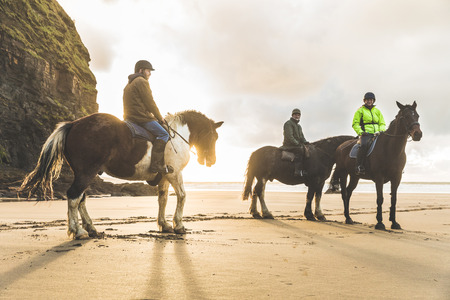 People with horses on the beach on a cloudy day. Three people restinf after riding horses. Epic photo with beautiful backlight. Sport and travel conceptsの写真素材