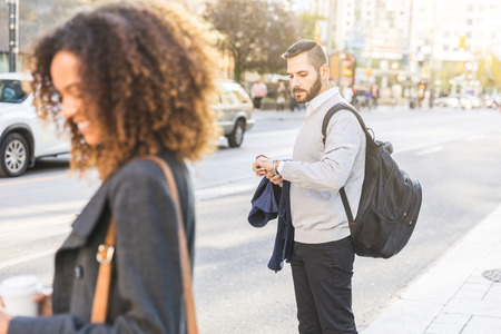 Man looking at watch and waiting by the street. Modern businessman wearing smart casual clothes in the city. Blurred woman on foreground. Urban lifestyleの写真素材