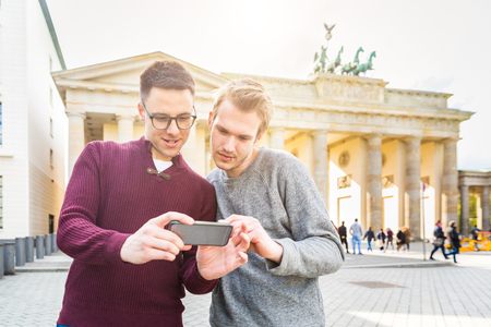 Two men looking at a smartphone in Berlin. Two friends in the city with Brandenburg Gate on background. Lifestyle, friendship and tourism concepts with real people models.の写真素材
