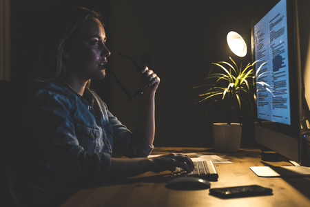 Young woman working at computer station at home. Beautiful girl looking at the monitor, sitting and...