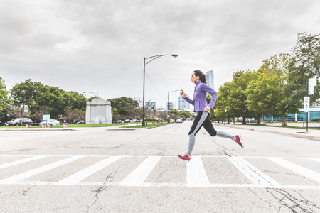 Woman jogging and crossing the road on zebra in Chicago. Beautiful mixed race woman wearing warm...