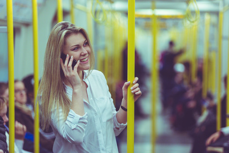 Young woman talking on the phone while commuting by tube train in London. Beautiful blonde girl...