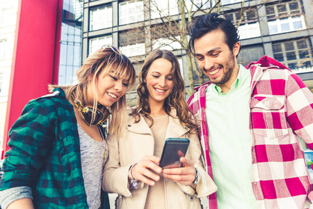 Friends with smartphone in the city. Multiethnic group of people, best friends, looking at mobile phone and smiling. Friendship, lifestyle and technology concepts.の写真素材