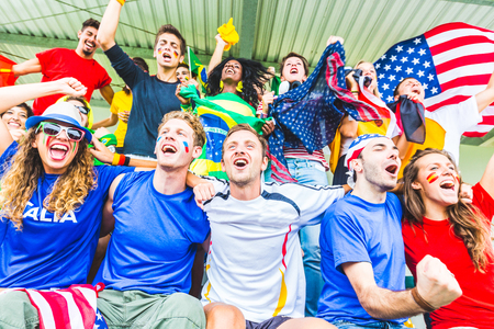 Supporters at stadium coming from different countries. Group of people enjoying sport match all together, with flags and colourful tshirtsの写真素材