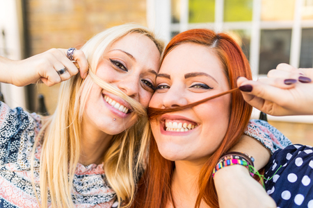 Girls making mustaches with hair. Happy and smiling young women playing with hair and pretending to have mustaches. Friendship and lifestyle conceptsの写真素材