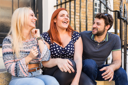 Group of friends talking and laughing together. Best friends, two girls and a boy, sitting in front of house and having fun. Lifestyle and friendship conceptsの写真素材