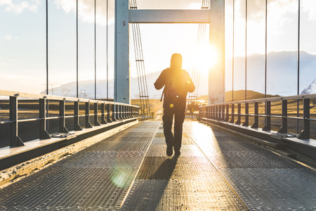 Man walking on bridge at sunset. Explorer with backpack walking in Iceland on a journey through nature. Backlight shot with real sun flares. Adventure and wanderlust conceptsの写真素材