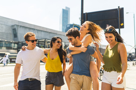 Multiracial group of friends together in the city. Multi ethnic group in London, walking on pavement on a sunny day. Man giving a piggyback ride to a girl. Friendship and lifestyle conceptsの写真素材