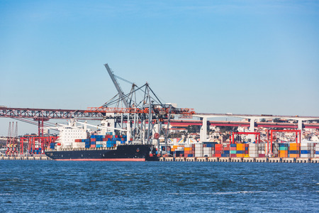 Cargo ship loading containers in Lisbon port. Large freight docked on a sunny day, delivering goods and loading before leaving. Transport and deliveries conceptsの写真素材