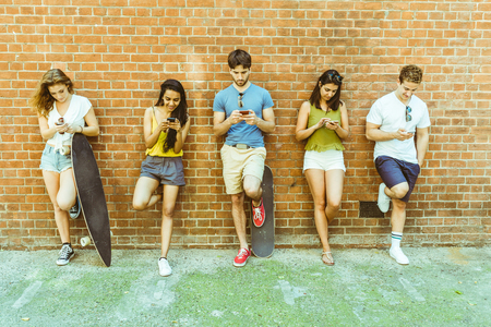 Group of friends using smartphone not interested in each other. Five persons leaning to a wall and...