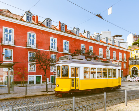Tram 28, the famous yellow tram in Lisbon on a sunny day, with a red building on background. Summer postcard from Portugal, toned image. Travel and architecture conceptsのeditorial素材