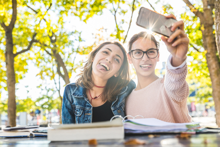 Girls studying together at park and taking a funny selfie. Happy best friends with books having fun while studying. Friendship and lifestyle concepts.の写真素材