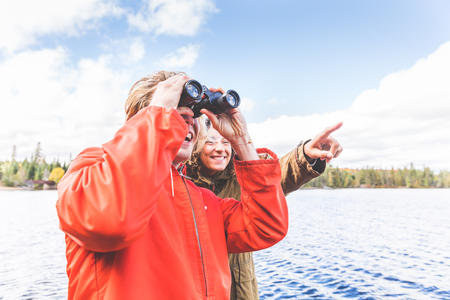 Happy couple looking through a binoculars. The man is holding the binoculars, the woman is standing next to him and looking away. Exploration and nature conceptsの写真素材