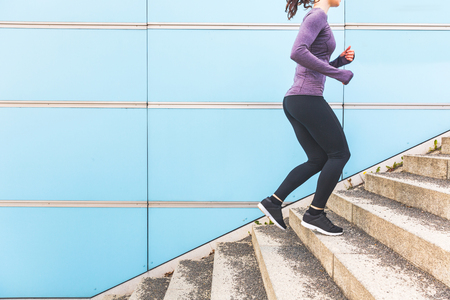 Woman jogging and running up a staircase. Girl wearing hi-tech clothes doing fitness activities outdoors. Healthy lifestyle and sport conceptsの写真素材