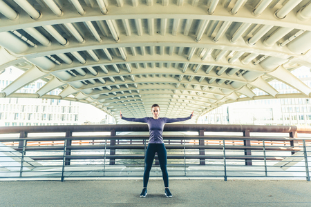 Woman doing stretching excercises, portrait with simmetry. Girl stretching arms during workout, simmetry with the architecture. Sport and fitness conceptsの写真素材