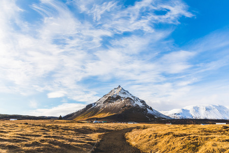 Mountain with snow in Iceland, winter landscape. Single mountain in the middle, clouds on top and yellow grass on foreground. Travel and winter conceptsの写真素材