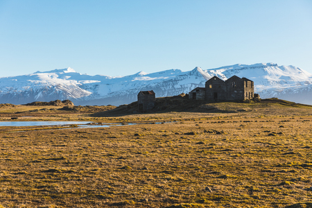 Iceland bleak landscape with ruined houses on foreground and snow covered mountains on background. Travel and winter concepts, wild Icelandic place.の写真素材