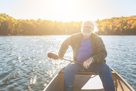 Senior man with canoe rowing on a sunny day. Man canoeing on a lake in Ontario, Canada. Typical outdoor activity, travel and leisure conceptsの写真素材