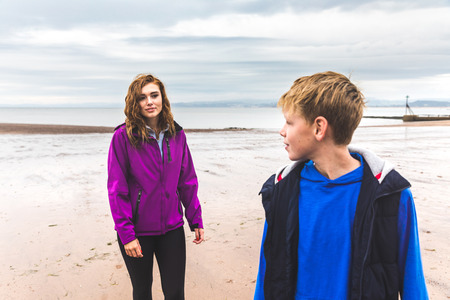 Boy and girl at beach on a rainy day. Siblings or friends walking and looking each other on a moody...