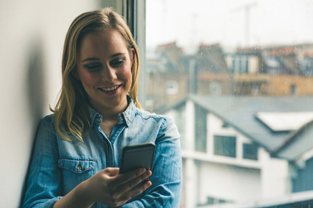 Beautiful blond girl wearing denim shirt checking her smartphone.の写真素材