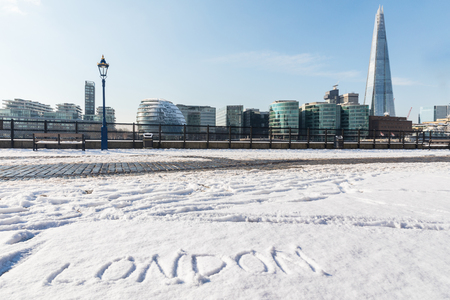 London cityscape view with snow on a sunny day. London written on the snow in foreground with modern buildings on background. Travel and weather conceptsの写真素材