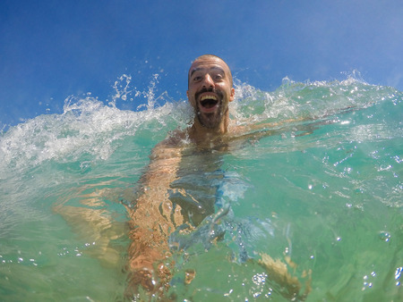 Man having fun with waves at seaside in Spain. Young man taking a selfie part underwater at seaside...