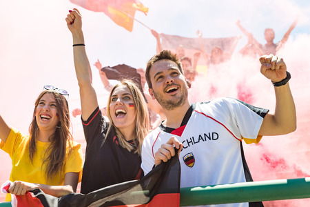 German supporters celebrating at stadium for football match. Group of fans and friends watching a match and cheering team Germany for international competition. Sport and lifestyle concepts.の写真素材