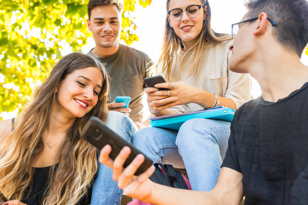 Teen group of friends with smartphones at park. Millennials best friends using mobile phones, addicted to technology and social media. Lifestyle and friendship conceptsの写真素材