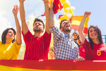 Spanish supporters cheering clapping hands at stadium. Group of fans watching a match and cheering team Spain with flags and chants. Sport and lifestyle concepts.の写真素材
