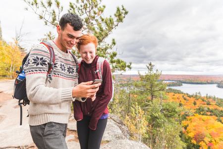 Couple hiking in Ontario during colorful fall season and checking smartphone or gps for map or photos. Travel and adventure concepts, caucasian man and woman models.の写真素材