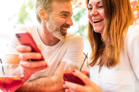 Adult couple dating and having a drink in Barcelona. Man and woman together at a bar in Barcelona, looking at a phone and laughing. Love and lifestyle conceptsの写真素材