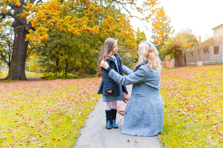Mother and daughter at park in autumn in London. Mom and girl wearing warm clothes, main colors are yellow and orange, autumn season.の写真素材