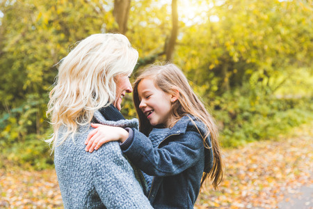 Mother and daughter playing and looking each other at park in autumn. Caucasian mom carrying her...