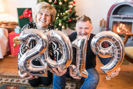 Happy senior couple celebrating new year 2019. Adult man and woman smiling, laughing and holding 2019 balloon sign on new year's eve celebrations. Lifestyle and holidaysの写真素材