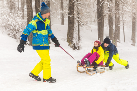 Friends having fun on the snow sliding with a little sled. Girl being pushed by two boys on a sledge. Winter sports and settings, white snow on the Italian Alpsの写真素材